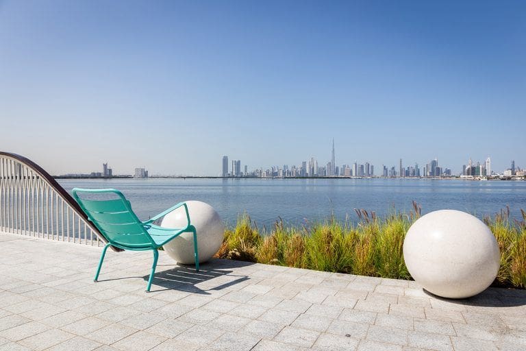 Green chair on a promenade overlooking Dubai Downtown with Burj Khalifa building and Dubai Creek