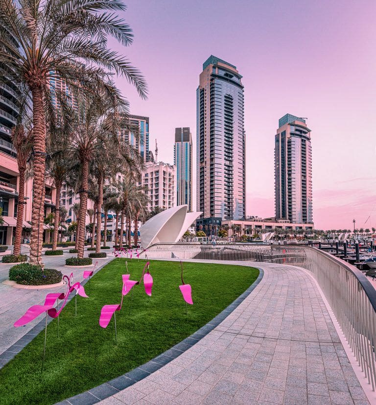 decorative figurines of pink flamingos on the boardwalk against the background of the bay with ships and yachts in the marina Creek Harbor in Dubai