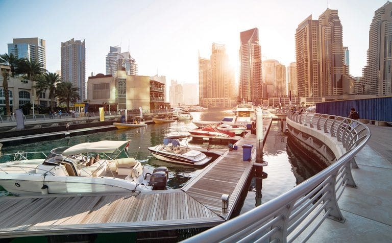 Panoramic view with modern skyscrapers and water pier of Dubai Marina at sunset